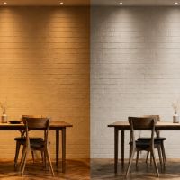 The same dining room shown twice side by side, lit by warm light on the left and cooler white light on the right, with the brick wall, wood table and floor reading differently in each half.