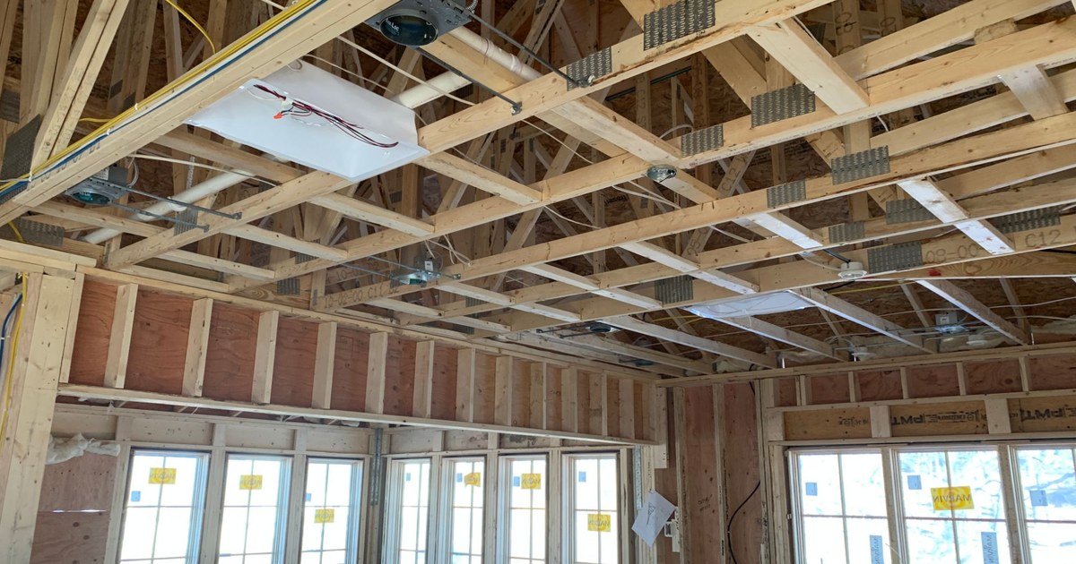 Open framed room during new construction, with exposed ceiling trusses, low-voltage wiring, speaker rough-in brackets, and junction boxes visible before drywall.