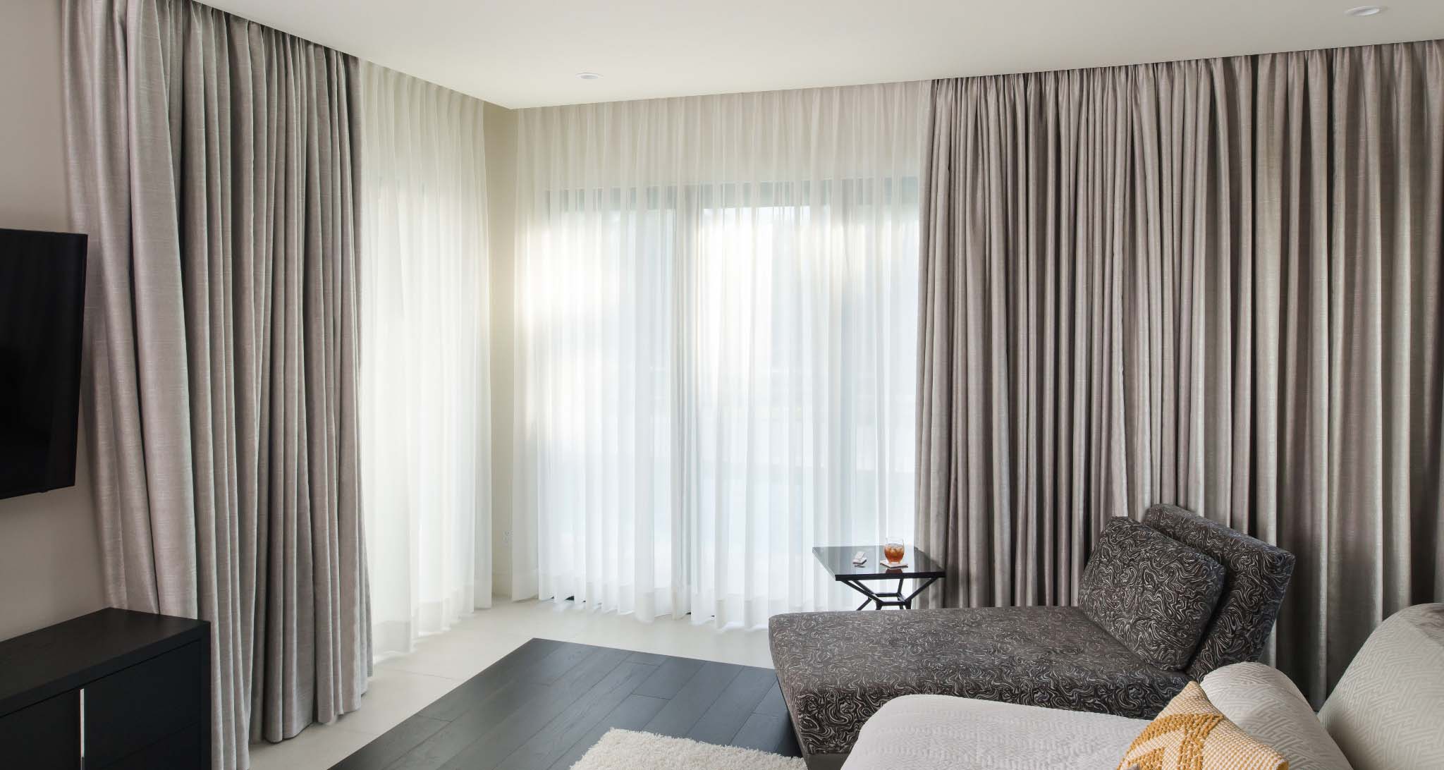 Bedroom with sheer and blackout drapery covering floor to ceiling windows