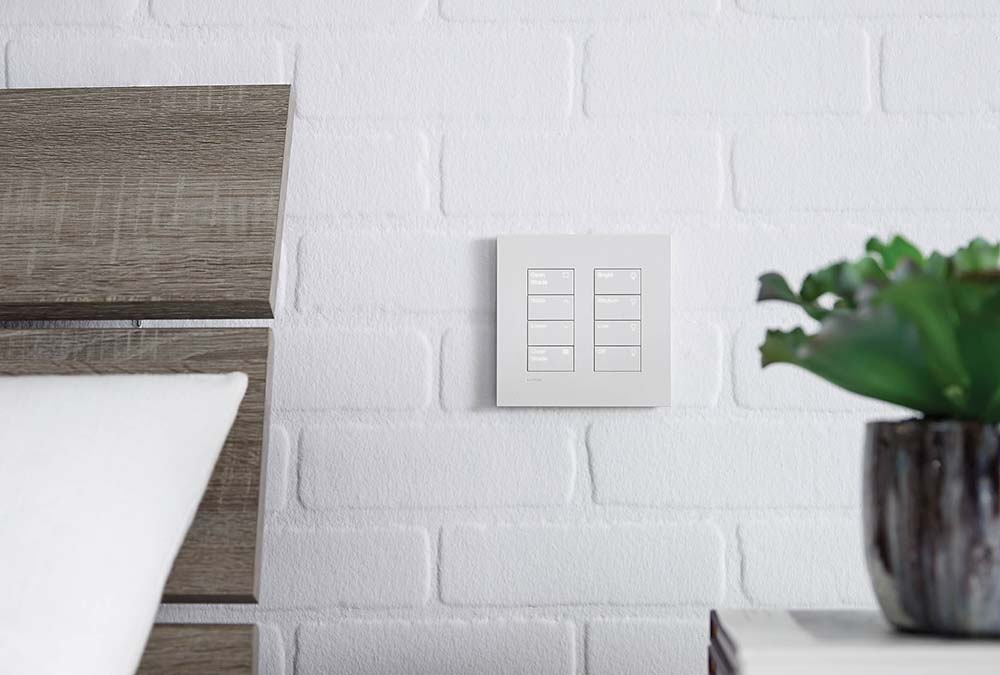 Wall keypad beside a wood headboard in a bright bedroom