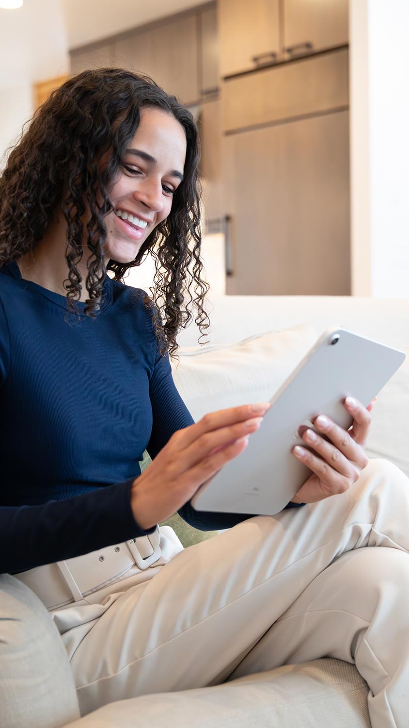 Smiling woman sitting on couch using tablet indoors