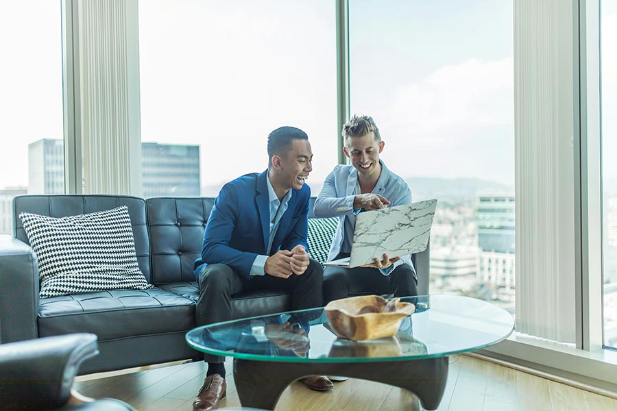 Two men in suits reviewing laptop together in bright office lounge