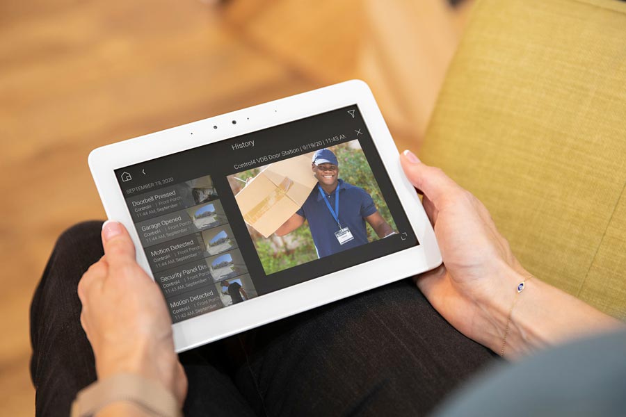 A woman holds a tablet in her hands as she looks at a security camera feed of a package delivery.