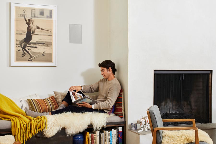 Person reading in a living room with an in-wall speaker behind him.
