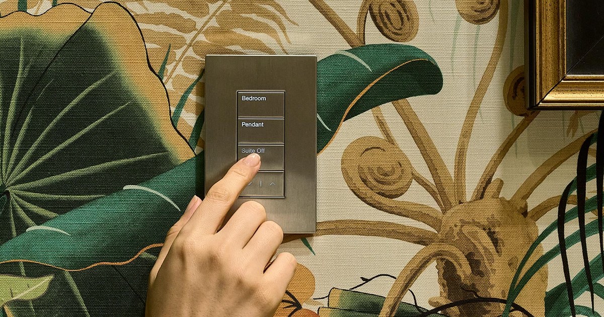 A hand pressing a bronze wall keypad with engraved buttons labeled Bedroom and Pendant.