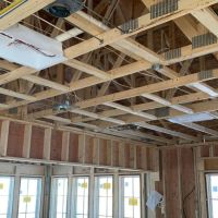 Open framed room during new construction, with exposed ceiling trusses, low-voltage wiring, speaker rough-in brackets, and junction boxes visible before drywall.