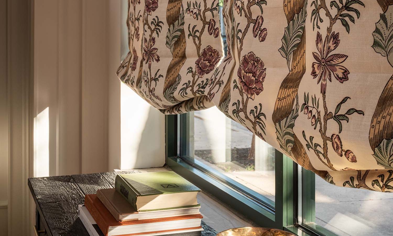 Patterned fabric shades hanging above a window with sunlight filtering through