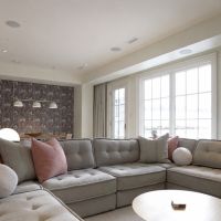A living room with a sectional sofa and three flush in-ceiling speakers, with snow visible through the windows.