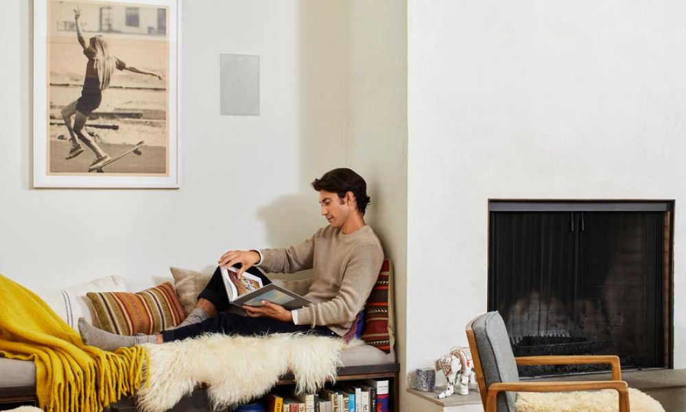 <span class="uk-h4">Person reading in a living room with an in-wall speaker behind him.</span>