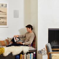 Person reading in a living room with an in-wall speaker behind him.