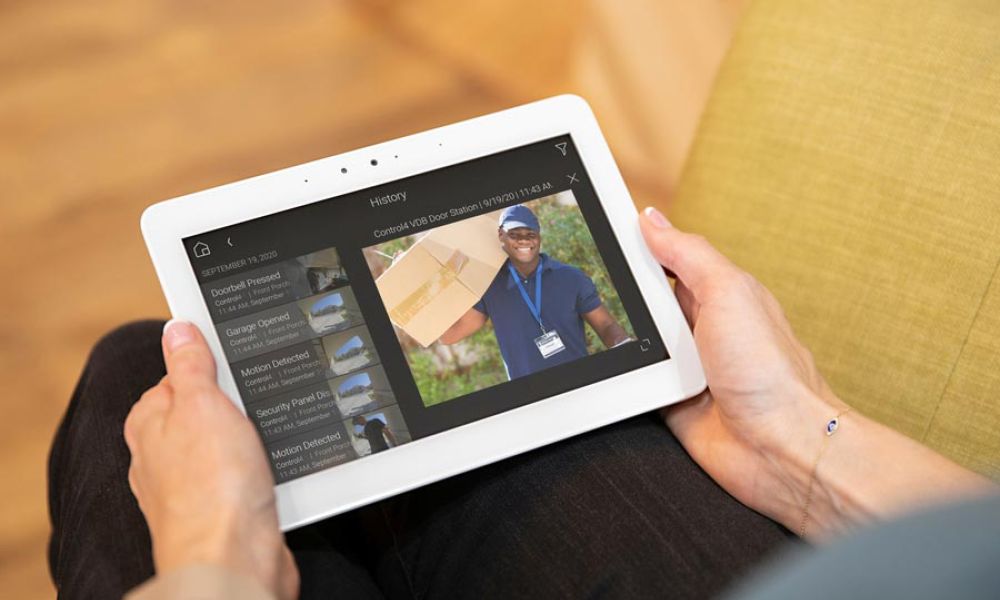 <span class="uk-h4">A woman holds a tablet in her hands as she looks at a security camera feed of a package delivery.</span>