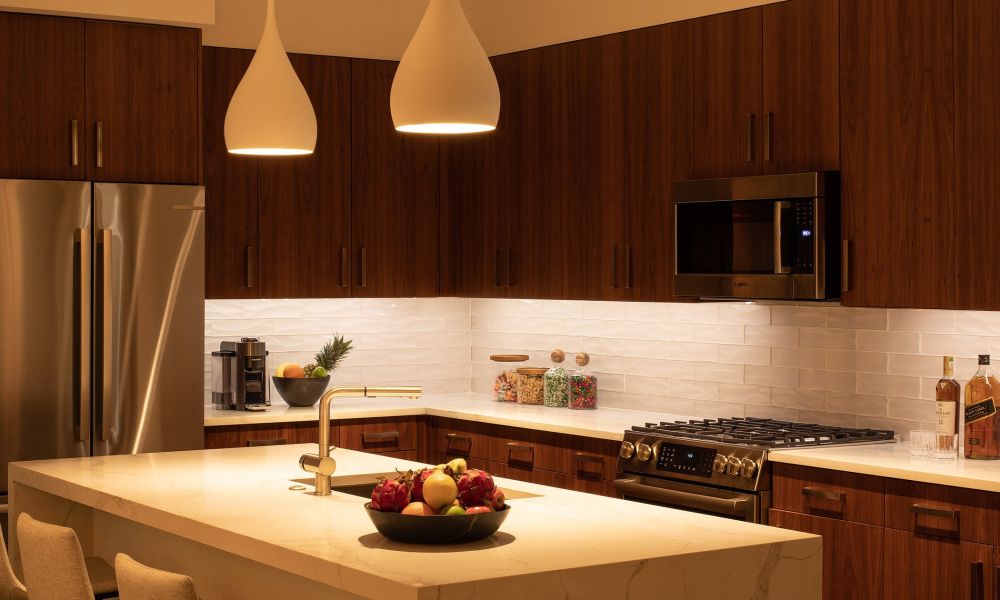 <span class="uk-h4">A kitchen at night with warm under-cabinet lighting along the counters and two pendant lights over the counter run, in a room of dark walnut cabinets and a white quartz island.</span>